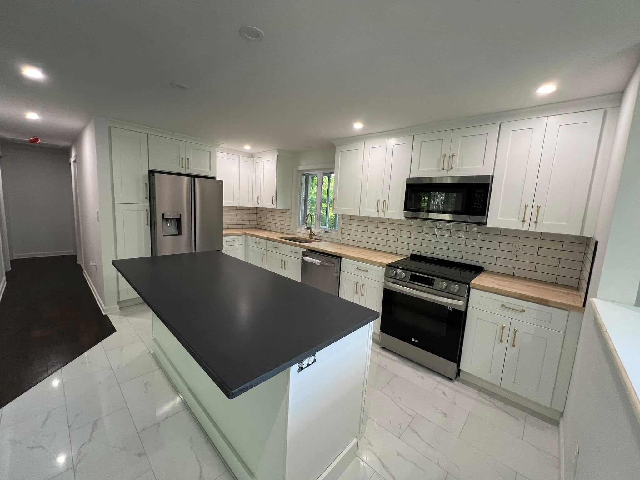 Kitchen Remodel in Andover Connecticut Modern kitchen with white shaker cabinets, light wood countertops, and stainless steel appliances. Features a black countertop island, subway tile backsplash, and recessed lighting. The kitchen has a clean, bright design with white marble-look tile flooring. Located in Andover, Connecticut.